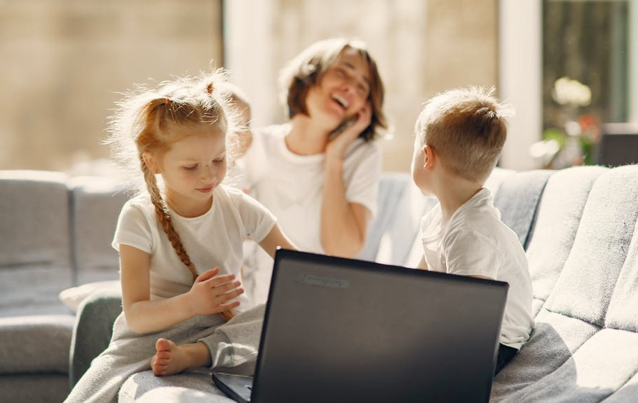 How to Work From Home And Make Money Online - Young Mother laughing with her 3 children in front of a laptop computer at home. 